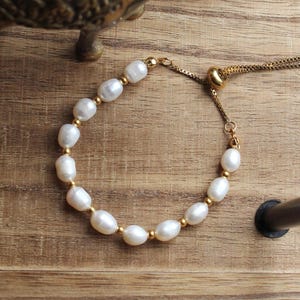 May include: A white pearl bracelet with a gold adjustable clasp. The bracelet is made of small, round pearls and a delicate gold chain.