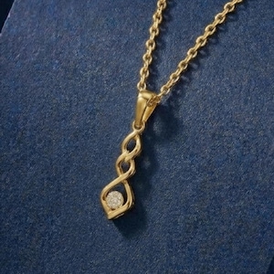 Könnte beinhalten: Eine goldfarbene Halskette mit einem Anhänger in verschlungenem Design und einem kleinen, klaren Edelstein. Die Kette ist filigran, und der Anhänger hängt vor einem dunkelblauen Hintergrund.