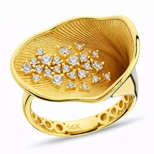 May include: A gold ring with a textured, fan-shaped design, adorned with numerous clear gemstones. The ring's band is also gold, with a series of circular cutouts. The ring is stamped with "14K".