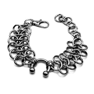 May include: A silver-toned chainmail bracelet with a lobster clasp closure. The bracelet features multiple rows of interlocking circular links, creating a textured, industrial design. Two small, round beads are attached to the central portion of the bracelet.