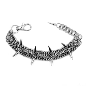 May include: A silver-colored chainmail bracelet with pointed spikes. The bracelet features a lobster clasp closure and a chainmail design. The spikes are evenly spaced along the bracelet's length, creating a bold, edgy look. The bracelet is designed for wrist wear.