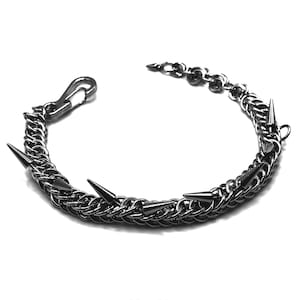 May include: A silver-toned chain bracelet with multiple pointed spikes. The bracelet features a hook clasp and a series of small chain links. The spikes are evenly spaced along the main chain, creating a bold, edgy aesthetic. The bracelet is set against a white background.