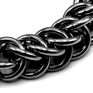 May include: Close-up of a silver chain link necklace. The chain is made of interlocking, rounded metal links. The links are highly reflective, with highlights and shadows creating a sense of depth. The background is white.