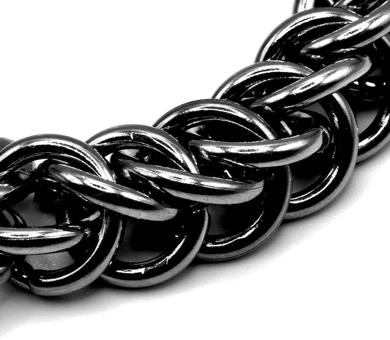 May include: Close-up of a silver chain link necklace. The chain is made of interlocking, rounded metal links. The links are highly reflective, with highlights and shadows creating a sense of depth. The background is white.