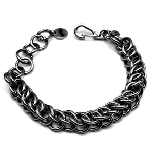 May include: A dark gray chainmail bracelet with a lobster clasp closure. The bracelet features a series of interconnected, rounded links, creating a textured, industrial look. The bracelet is shown against a white background.