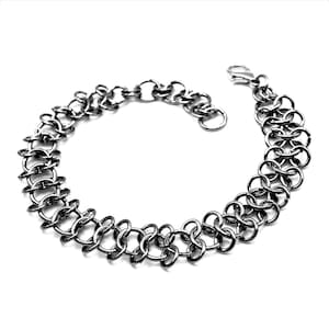 May include: A silver-colored chain bracelet with a series of interconnected oval and round links. The bracelet has a clasp closure and is displayed against a white background. The jewelry is a fashion accessory.