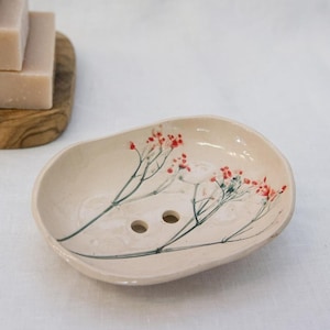 Könnte beinhalten: Eine weiße Keramik-Seifenschale mit Blumenmuster. Die Schale hat zwei Abflusslöcher und ist mit gepressten roten und grünen Blumen verziert.