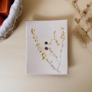 Może przedstawiać: Biała ceramiczna mydelniczka z kwiatowym wzorem. Mydelniczka ma dwa otwory odpływowe i jasnobrązowy wzór kwiatowy.