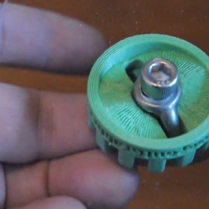 May include: A green plastic 3D printed gear with a silver metal bolt and nut in the center.