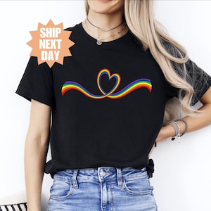 May include: A black t-shirt with a rainbow heart design. The rainbow is in the colors of the pride flag.