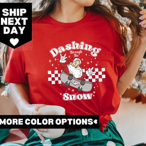 May include: Red t-shirt with a graphic of Santa Claus skateboarding with the text "Dashing through the snow" in a retro font.