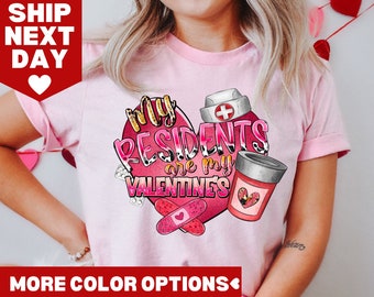 Op de afbeelding: Lichtroze T-shirt met een Valentijnsdagontwerp. De afbeelding bevat een hart met de tekst "My Residents are my Valentine's" en afbeeldingen van een verpleegstershoed, pillen en een medicijnfles.