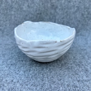 Small off white hand built speckled pottery bowl with unique carved texture
