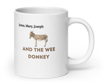 Könnte beinhalten: Weiße Keramiktasse mit einer braunen Esel-Illustration und dem Text "Jesus, Mary, Joseph AND THE WEE DONKEY".