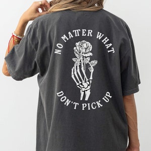 May include: A dark gray t-shirt with a white graphic on the back. The graphic features a skeleton hand holding a rose with the text "No matter what don't pick up".