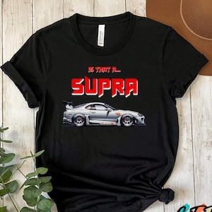 May include: Black t-shirt with a white Toyota Supra car graphic and the text "Is that a... Supra" in red.