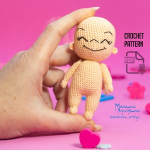 May include: A crocheted doll with a smiling face and closed eyes. The doll is light peach in color and is being held by a hand. The background is pink. The text "CROCHET PATTERN" and "PDF" are visible in the image.