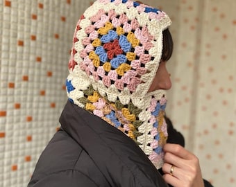May include: A white crocheted hooded scarf with a granny square pattern in pink, blue, yellow, and green.