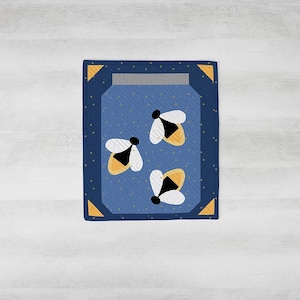 May include: A blue and gold quilt featuring a jar design with three stylized fireflies. The fireflies have white wings and yellow and black bodies. The quilt has a dark blue border with gold corner accents.