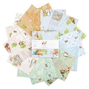 May include: A collection of fabric squares featuring illustrations of Peter Rabbit and other characters from the children's book series. The squares are in various pastel colors, including blue, green, and tan, with printed text and images.