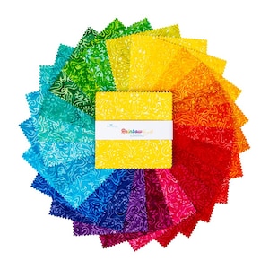 May include: A collection of colorful fabric squares arranged in a circular pattern, showcasing a spectrum of hues from blue to red. The squares are patterned with a swirling design. A yellow stack of squares is wrapped with a white band that reads "Rainbow Elements".