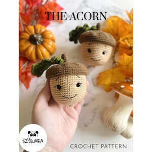May include: Crocheted acorn with a smiling face, brown cap, and green leaf. The image includes the text "THE ACORN" and "CROCHET PATTERN". Other fall-themed crochet items are in the background.