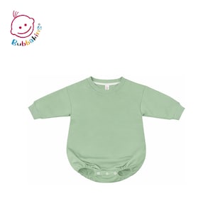 Könnte beinhalten: Ein langärmeliger Baby-Strampler in Salbeigrün mit rundem Halsausschnitt, gerippten Bündchen und einem Druckknopfverschluss im Schritt. Das Kleidungsstück wird mit dem Bubbakins-Logo in der oberen linken Ecke gezeigt, das ein stilisiertes Babygesicht zeigt.