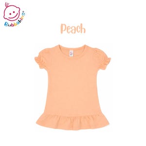 K&ouml;nnte beinhalten: Ein einfarbiges, pfirsichfarbenes Kurzarmshirt mit Rundhalsausschnitt, gerafften Puff&auml;rmeln und einem ger&uuml;schten Saum. Das Bubbakins-Logo ist oben links zu sehen und das Wort Peach steht mittig &uuml;ber dem Shirt abgebildet.