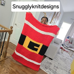 Può includere: Una coperta lavorata a maglia rossa, bianca, nera e gialla con la scritta "Snugglyknitdesigns". La coperta è progettata per assomigliare al costume di Babbo Natale, con una cintura nera e una fibbia gialla. La coperta è fatta di filato spesso.