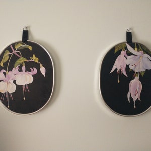 May include: Two round framed prints with black backgrounds and pink and white flowers. The flowers are painted in a realistic style and have delicate details.