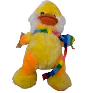 May include: A yellow and orange plush duck wearing a colorful striped scarf. The duck has a white fluffy head and a bright orange beak.