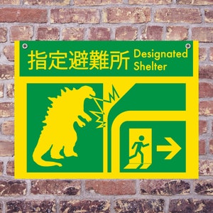 May include: A rectangular green and yellow sign with Japanese text and the English words "Designated Shelter." The sign features a yellow Godzilla-like creature and an exit symbol. The sign is mounted on a brick wall.