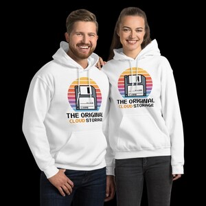 Op de afbeelding: Witte hoodies met een retro ontwerp van een diskette in een kleurrijke zonsondergangcirkel. De tekst "THE ORIGINAL CLOUD STORAGE" staat onder de afbeelding. Gedragen door twee personen.