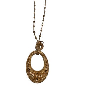 May include: A gold-toned necklace with an oval pendant. The pendant is intricately detailed with a textured surface and floral-like embellishments. The chain is delicate, and the pendant is suspended from a decorative clasp.
