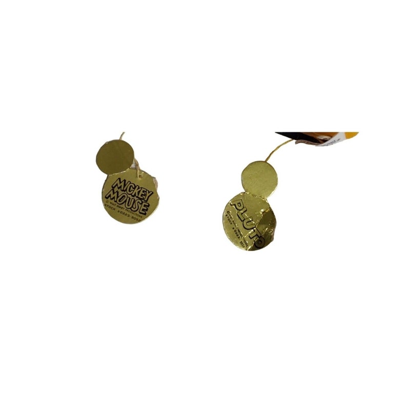 Op de afbeelding: Twee goudkleurige labels met de tekst "MICKEY MOUSE" en "PLUTO" in zwart gedrukt. De labels zijn met een dun gouden touwtje aan een product bevestigd. De labels zijn rond met een kleinere cirkel.