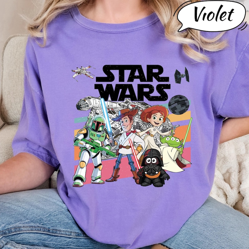 May include: A violet t-shirt featuring the text "STAR WARS" in black block letters. The shirt has a graphic of Star Wars characters and other cartoon characters. The word "Violet" is in a speech bubble.