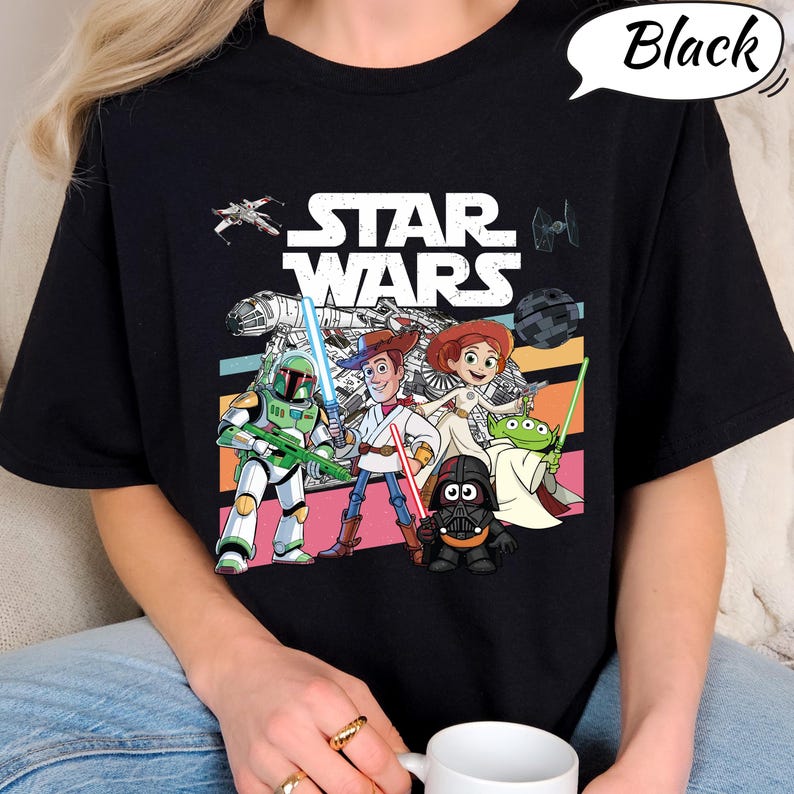 May include: Black t-shirt featuring a colorful graphic of Star Wars characters, including Boba Fett, Woody, Jessie, and Darth Vader. The Star Wars logo is prominently displayed above the characters, with a speech bubble that says "Black".