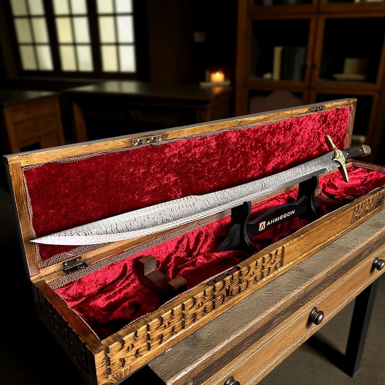 May include: An ornate sword with a patterned blade is displayed in an open wooden box lined with red velvet. The box features carved details. The sword rests on a black stand with the text "AHMEGON".