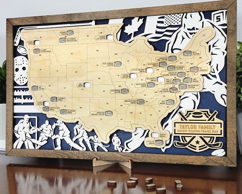 Pu&ograve; includere: Una mappa in legno degli Stati Uniti con gli stadi di hockey contrassegnati da rondelle. La mappa &egrave; incorniciata in una cornice di legno marrone e ha uno sfondo blu. Il testo "TAYLOR FAMILY HOCKEY STADIUM TRAVEL MAP" &egrave; in fondo alla mappa.