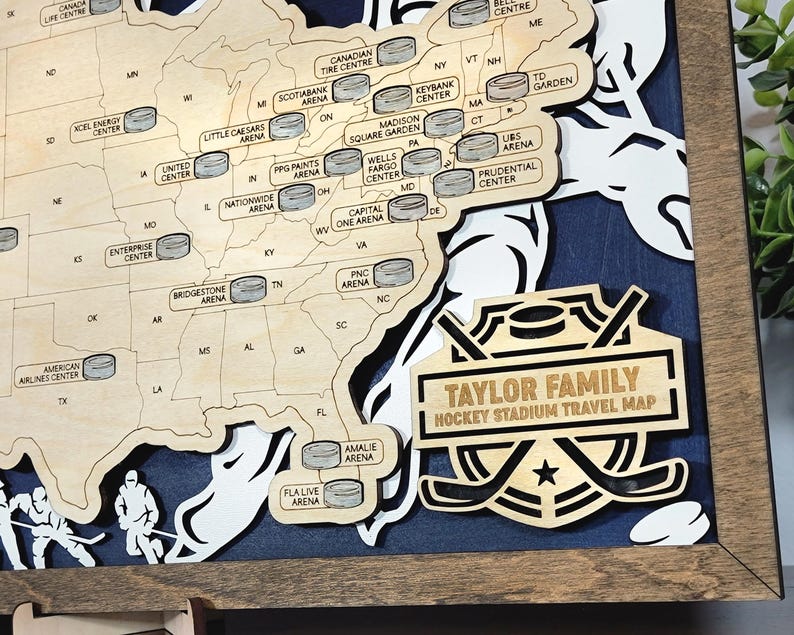 Pu&ograve; includere: Una mappa in legno degli Stati Uniti con gli stadi di hockey contrassegnati da icone a forma di disco. La mappa &egrave; incorniciata in legno e ha una targa dorata con il testo "Taylor Family Hockey Stadium Travel Map".