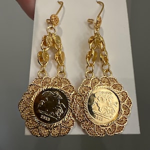 Puede incluir: Pendientes colgantes dorados con colgantes en forma de moneda y detalles de filigrana intrincados. Los pendientes tienen un diseño floral alrededor de las monedas y están suspendidos de delicadas cadenas. Las monedas muestran el año 1913.