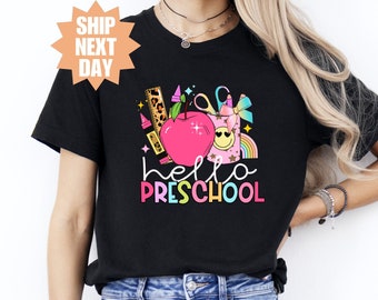 May include: Black t-shirt with a colorful graphic design featuring a red apple, rainbow, and the text "hello preschool".