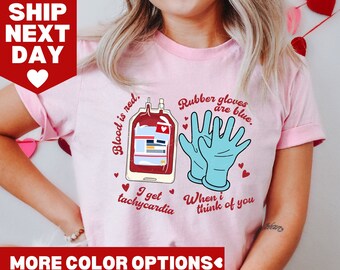 Op de afbeelding: Lichtroze T-shirt met een afbeelding van een bloedzak en blauwe rubberen handschoenen, met de tekst: "Bloed is rood. Rubberen handschoenen zijn blauw. Ik krijg tachycardie als ik aan je denk."