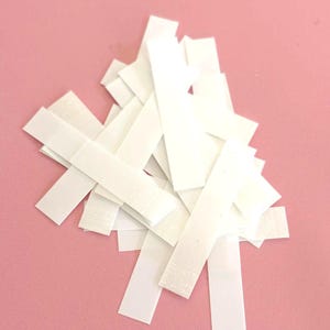 Puede incluir: Un montón de tiras de cinta adhesiva de doble cara blanca sobre un fondo rosa.