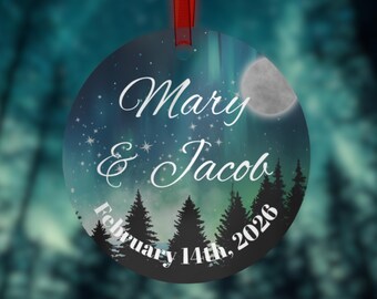 May include: Round ornament with a night sky design, featuring a full moon, stars, and a forest silhouette. The names "Mary & Jacob" and the date "February 14th, 2026" are written in elegant script. A red ribbon is attached for hanging.