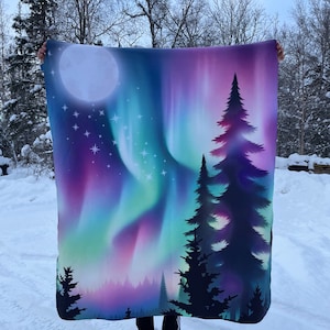 May include: A fleece blanket with a colorful aurora borealis design and a silhouette of a forest of pine trees. The moon is visible in the upper left corner of the blanket.