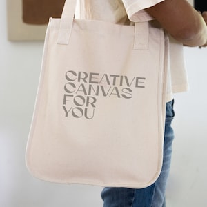 Puede incluir: Una bolsa de lona blanca con el texto "CREATIVE CANVAS FOR YOU" impreso en gris.