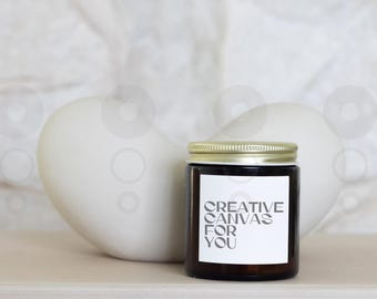 May include: A glass candle jar with a gold lid and a white label that reads "Creative Canvas For You".