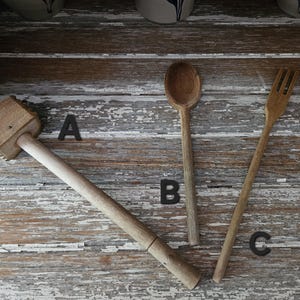 May include: Wooden kitchen utensils including a meat mallet, a spoon, and a fork. The mallet has a rectangular head and a long handle. The spoon has a rounded bowl, and the fork has three tines. All are made of light-colored wood.