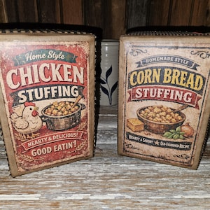May include: Two vintage-style boxes with the words "Chicken Stuffing" and "Corn Bread Stuffing" in bold lettering. The "Chicken Stuffing" box features a chicken illustration, while the "Corn Bread Stuffing" box has a bowl of stuffing. Both boxes have a rustic, aged appearance.